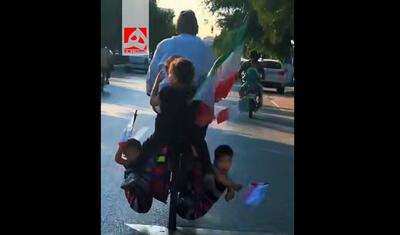  ۲ کودک پرچم به دست در خورجین دوچرخه پدر! + ویدئو | تصاویری که وایرال شد